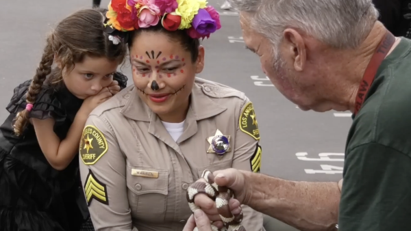 A LASD deputy in face paint looking at a man holding a snake at the Haunted Jailhouse event held on 10-27-2024