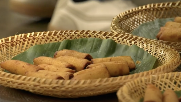 a the center of the image is a brown plate with a green napkin. On the plate is a dozen Lumpia egg rolls.