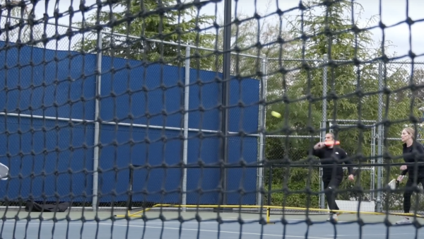 Three people seen through a black tennis net playing pickleball on the College of the Canyons Campus.