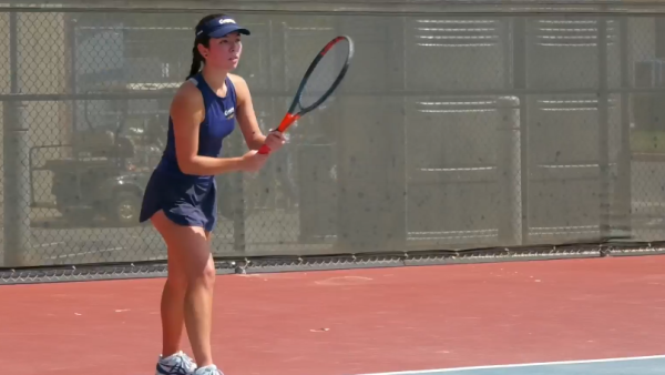 COC tennis athlete Estrella Segura dressed in dark blue stands ready to hit a tennis ball.