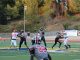 Hart quarterback Jacob in a gray and black uniform (number 2) preparing to throw the ball while being protected by his offensive line. Defensive players in white and red uniforms attempt to break through the blocks. A teammate wearing number 22 in gray is in the foreground, looking back toward the quarterback. The game is being played on a turf field with trees and a hillside in the background.