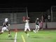 A Hart High School football player in a white uniform leaps to catch a pass during a night game against West Ranch, as a Wildcats defender closes in. The play takes place near the end zone with empty bleachers in the background.