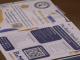 Flyers for college student support services lie on a table. One flyer promotes health and wellness workshops and includes a QR code, colorful graphics, and contact information. Another flyer advertises “The Basic Needs Center,” listing office hours, campus locations, available resources such as food assistance and school supplies, and another QR code. Social media icons and program details are visible across the pages.