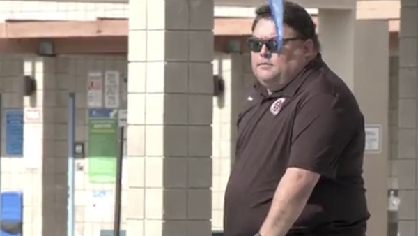 A Sean Kakumu sunglasses and a dark polo shirt stands outdoors near tiled columns and a railing, with a blue object partially obscuring the foreground.