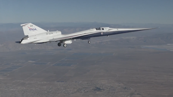 A sleek experimental NASA X-59 jet, marked with NASA branding, flies with its landing gear down over a vast desert landscape, with mountains faintly visible in the distance.