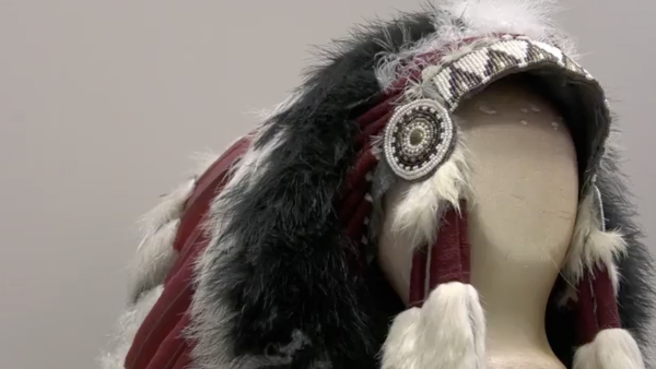 This image features a Native American-style headdress displayed on a neutral-toned mannequin head. The piece is highly detailed, showcasing traditional craftsmanship through various textures and materials.